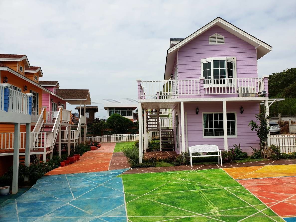 Un edificio residencial colorido con balcón, porche y una banca pequeña.