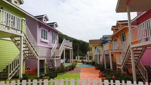 Una hilera de cabañas coloridas con escaleras exteriores, cerca de una valla de piquetes blancos y un césped bien cuidado.