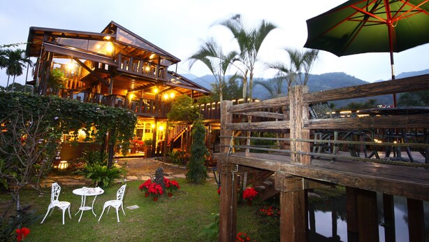A wooden house with a deck, outdoor seating, and a view of mountains. - Country Grange (Yuanshan)