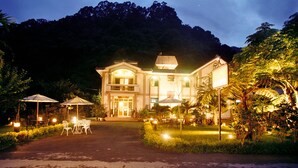 A large, well-lit building with a balcony, surrounded by lush greenery and a paved driveway. - Country Grange (Yuanshan)