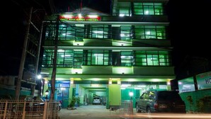A multi-story building with a green-lit entrance, a visible car parked outside, and a signboard above the entrance. - Nay Chi Linn Hotel (Pathein)