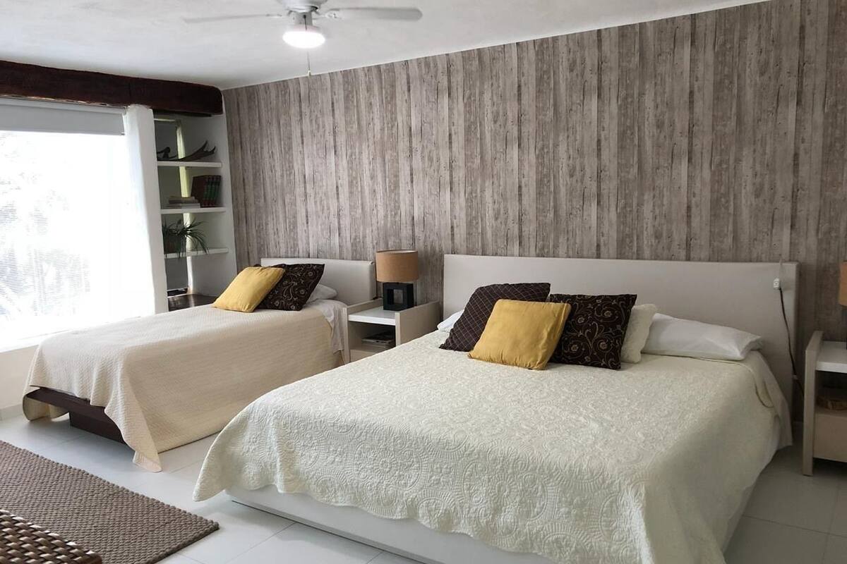 A modern bedroom with two beds, a wooden accent wall, and a ceiling fan.