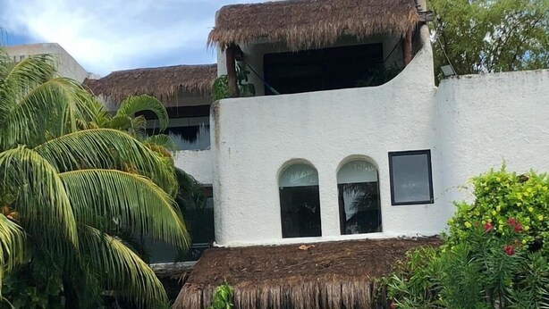 Un edificio de dos pisos con techo de paja, rodeado de abundante vegetación y palmeras.