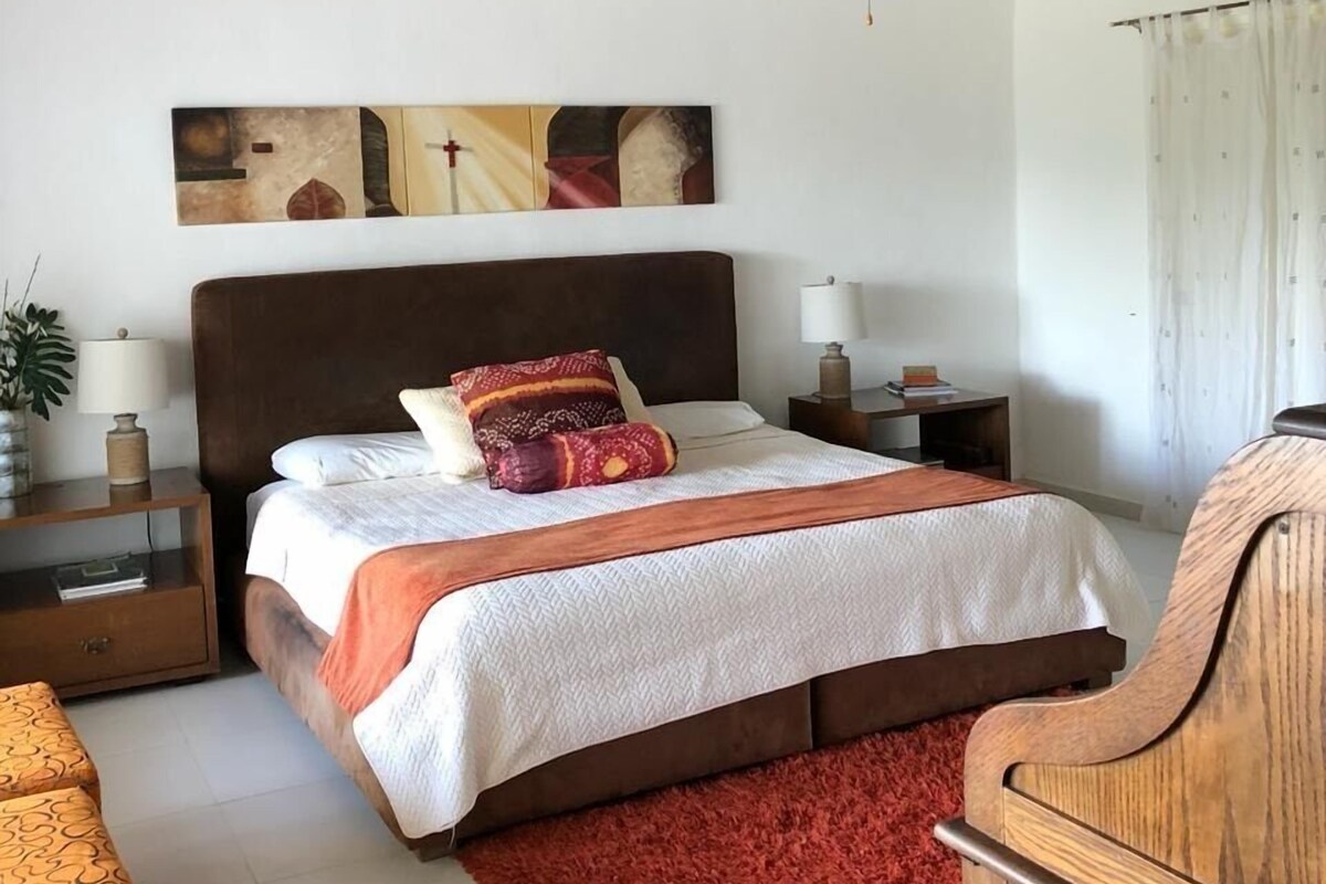 A bedroom with a bed, nightstands, a ceiling fan, and artwork on the wall.