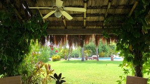 Un espacio al aire libre con mobiliario de mimbre y plantas en macetas, con vistas a un césped y una zona de piscina bien cuidados.