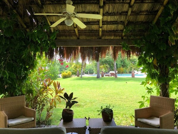 An outdoor seating area with wicker furniture and potted plants, overlooking a well-maintained lawn and pool area.