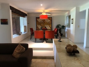 A modern living room with a dark sofa, a dining table with red chairs, and a staircase leading to another level.