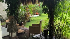 Un espacio de estar al aire libre cubierto con mobiliario de mimbre, plantas en macetas y techo de paja.