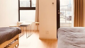 Ein kleines Hotelzimmer mit zwei Betten, einem Tisch und einem Fenster mit Vorhängen.