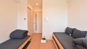 A small, modern room with two single beds, a wooden floor, and a small table in the center.