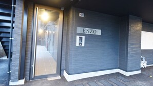Ein moderner Gebäudeeingang mit Glastür, Metalltreppe und einem Schild mit der Aufschrift 'ENZO'.