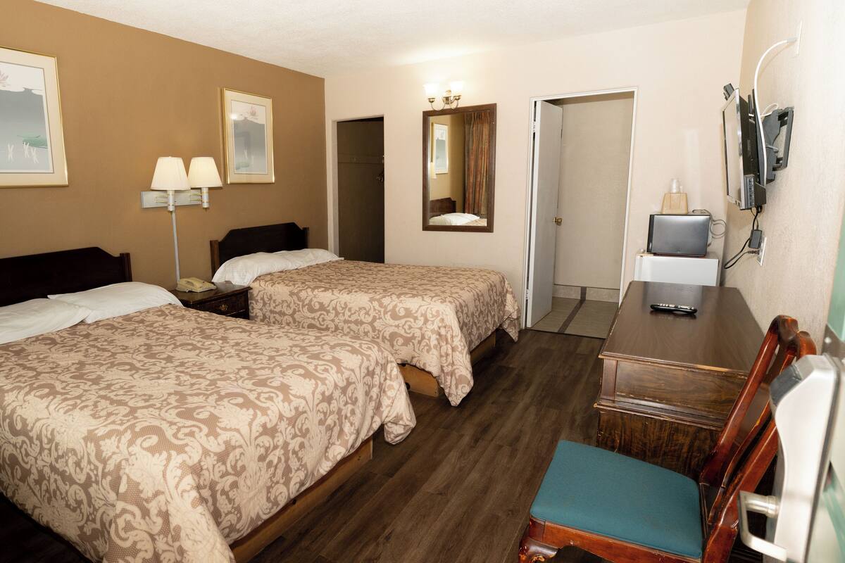 A hotel room with two beds, a desk, a chair, a TV, and a mirror.