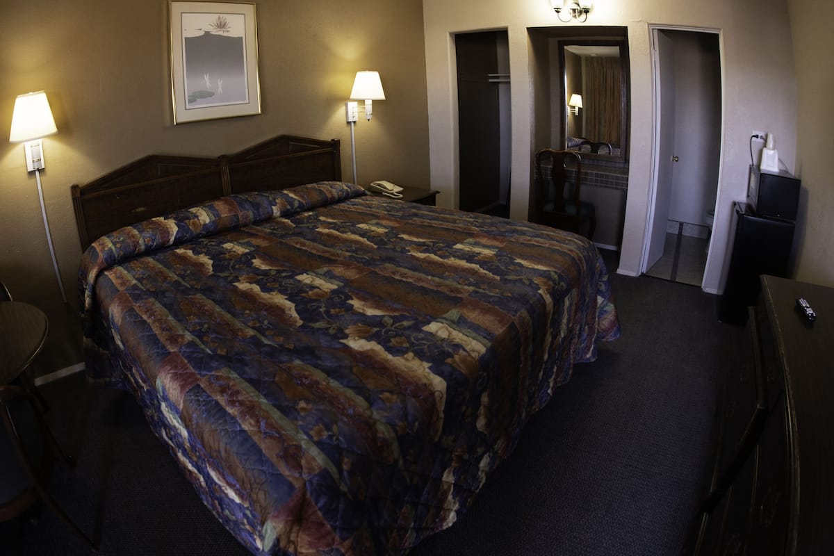 A hotel room with a large bed, two bedside lamps, a desk, a chair, a telephone, and a mirror.