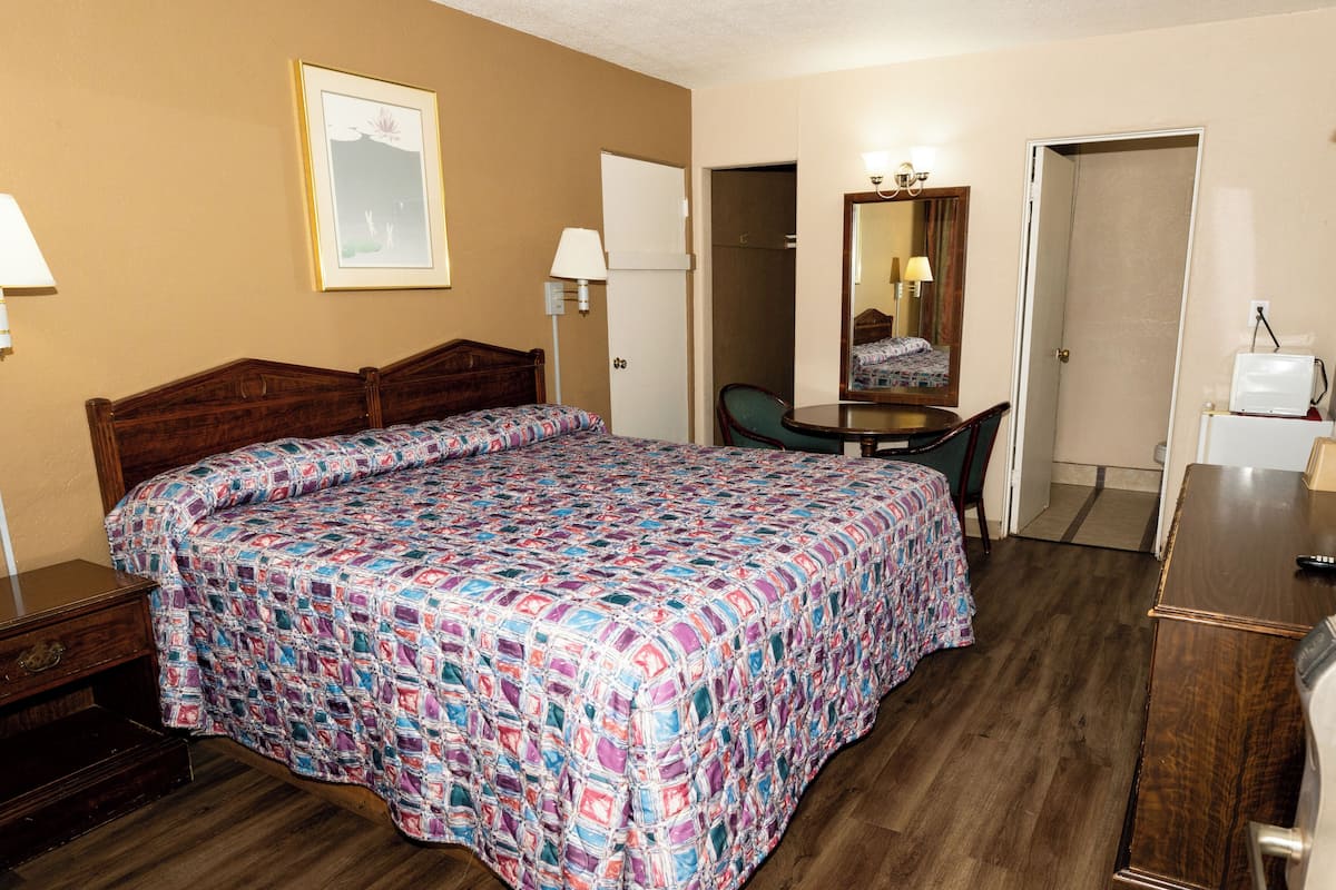 A hotel room with a large bed, a desk, a chair, a mirror, and a small table.
