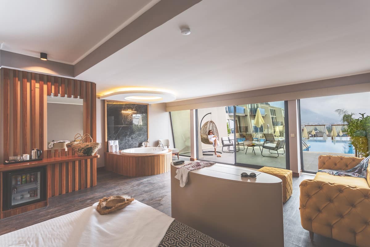Habitación de hotel moderna con una cama grande, una zona de estar con una mesa redonda, una bañera y vistas a la zona de la piscina exterior.