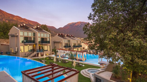 Un resort con múltiples piscinas, un área de terraza cubierta y montañas al fondo.