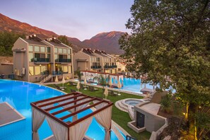 A resort with multiple swimming pools, a covered deck area, and a mountainous backdrop. - Orka Cove Hotel Penthouse & Suites - Adults Only (Fethiye)
