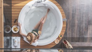 Una persona relajándose en un jacuzzi con un piso de madera alrededor.