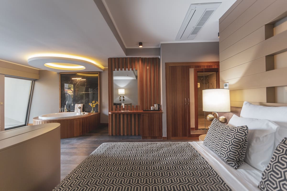 Una habitación de hotel moderna con una cama grande, un baño con bañera, un tocador con espejo y un escritorio con lámpara.