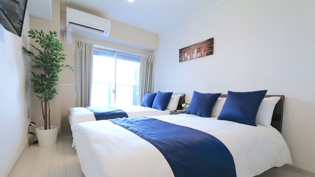 A hotel room with two beds, a potted plant, an air conditioning unit, and a window with curtains. - Elizabeth Garden Shinsaibashi (Osaka)