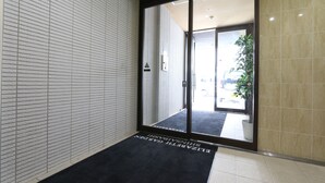 A hotel entrance with a sliding glass door, a black mat with "ELIZABETH GARDEN" text, and a tiled wall. - Elizabeth Garden Shinsaibashi (Osaka)