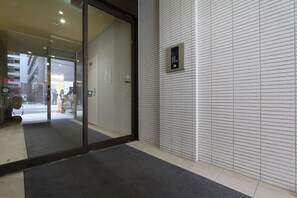 Ein Hotel Eingang mit Glastür, schwarzem Fußmatten und einem wandmontierten Aufzug Bedienfeld.