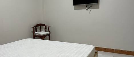 A bedroom with a bed, a chair, a television mounted on the wall, and a power outlet.