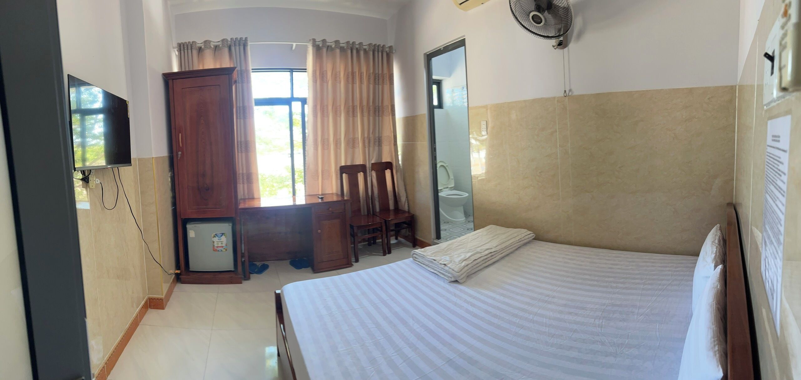 A hotel room with a bed, a desk, a chair, a wardrobe, a television, and a bathroom.