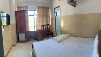 A hotel room with a bed, a desk, a chair, a wardrobe, a television, and a bathroom.