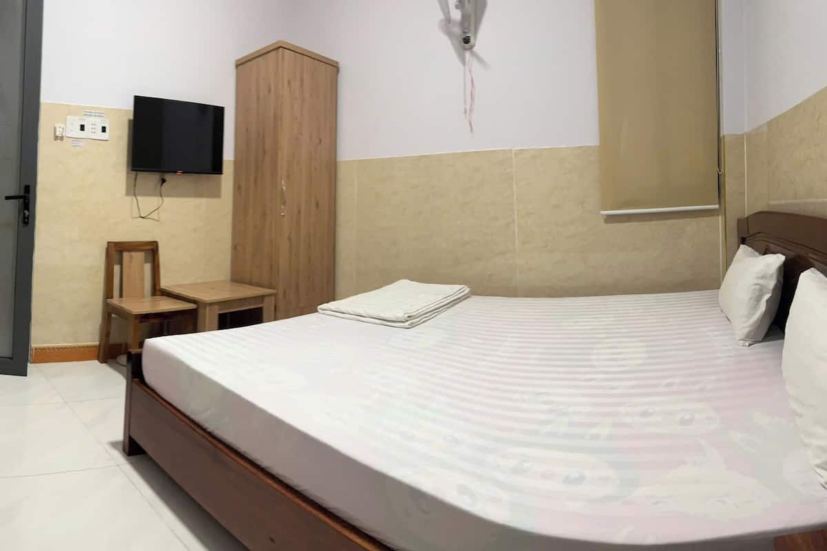 A bedroom with a bed, a television mounted on the wall, a wooden wardrobe, and a red chair.