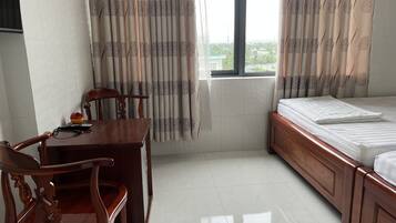 A hotel room with a wooden desk, a chair, a bed with a white mattress, and a window with curtains.