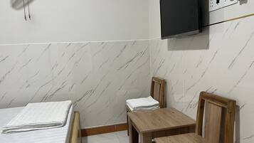 Ein Hotelzimmer mit einem Bett, einem Holztisch, einem Sessel, einem an der Wand befestigten Fernseher und einer Steckdose.