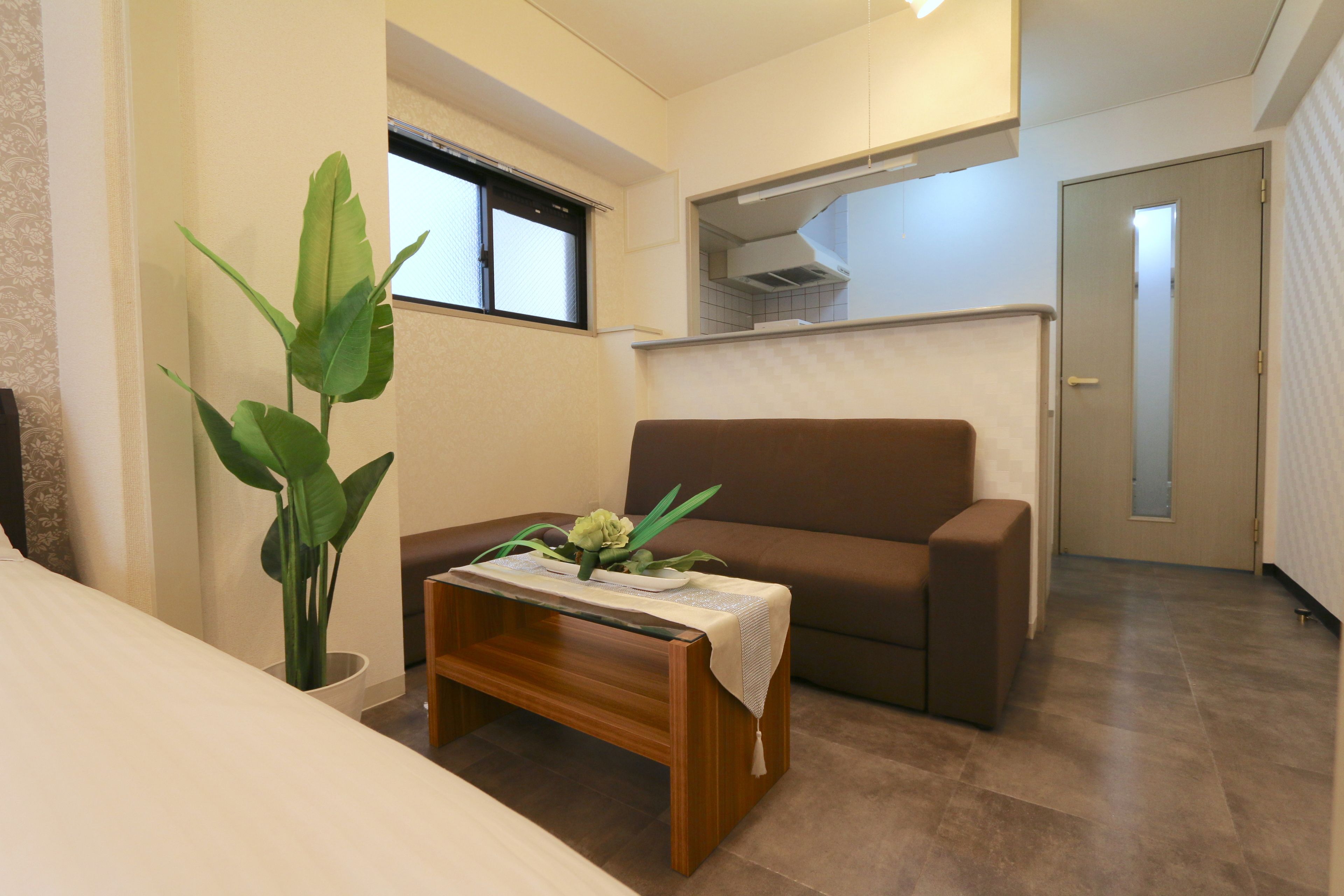 A modern living room with a brown sofa, a wooden coffee table with a plant, and a large window.