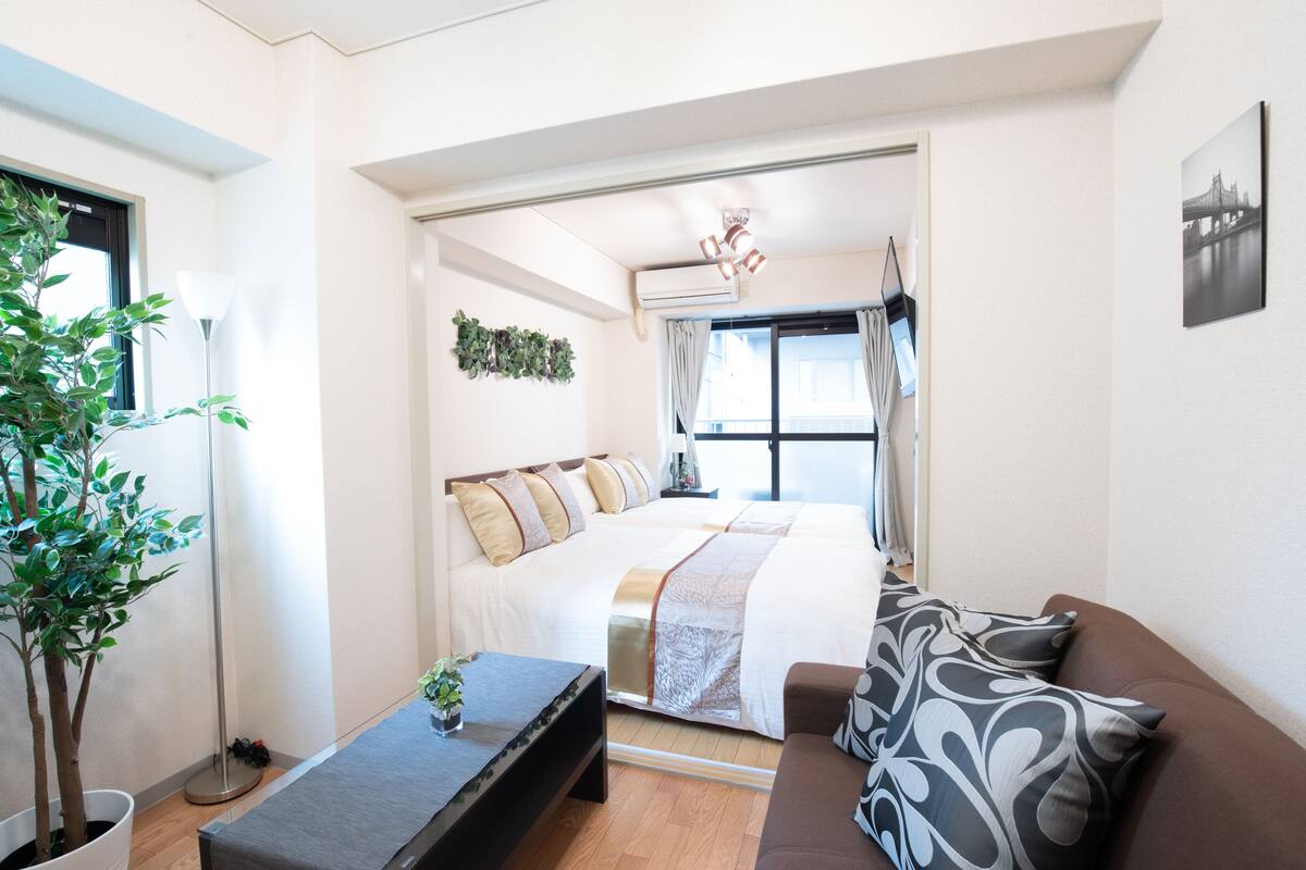 Une chambre à coucher moderne, avec un grand lit, une table de chevet, une plante en pot et une vue sur l’extérieur par une fenêtre.