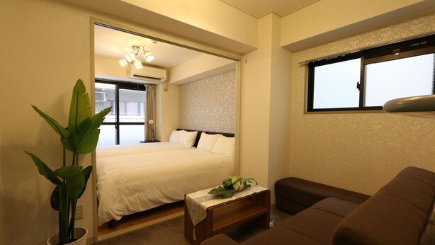 A bedroom with a bed, bedside table, and a potted plant. - Elizabeth Garden II (Osaka)