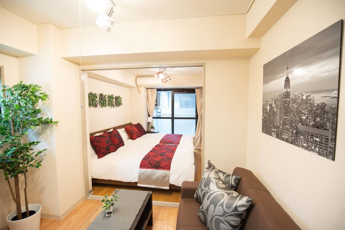 Une chambre d’hôtel avec un lit, un canapé, une plante en pot et un tableau représentant un paysage urbain.