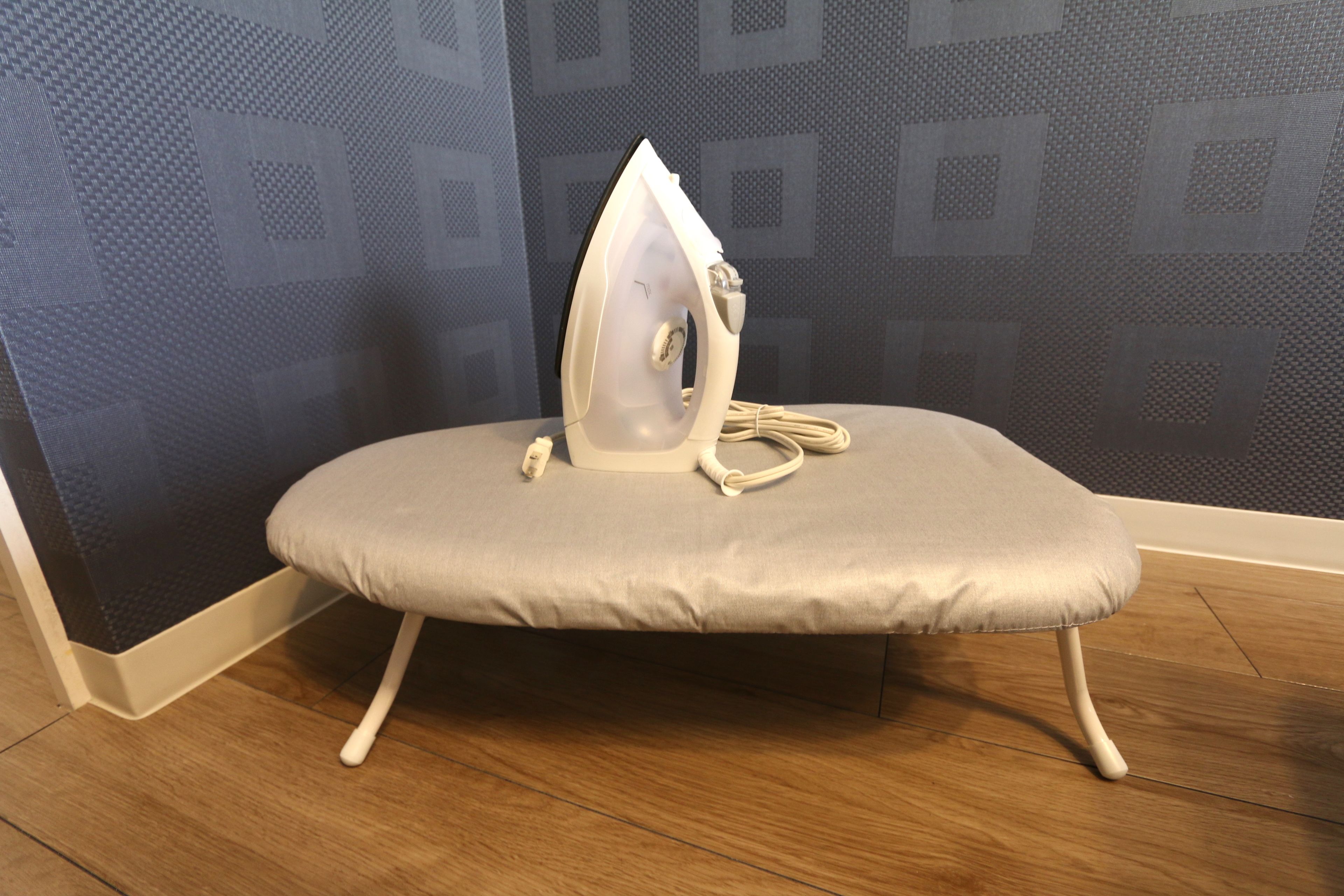 An ironing board with an iron placed on it, positioned against a wall with a geometric pattern.