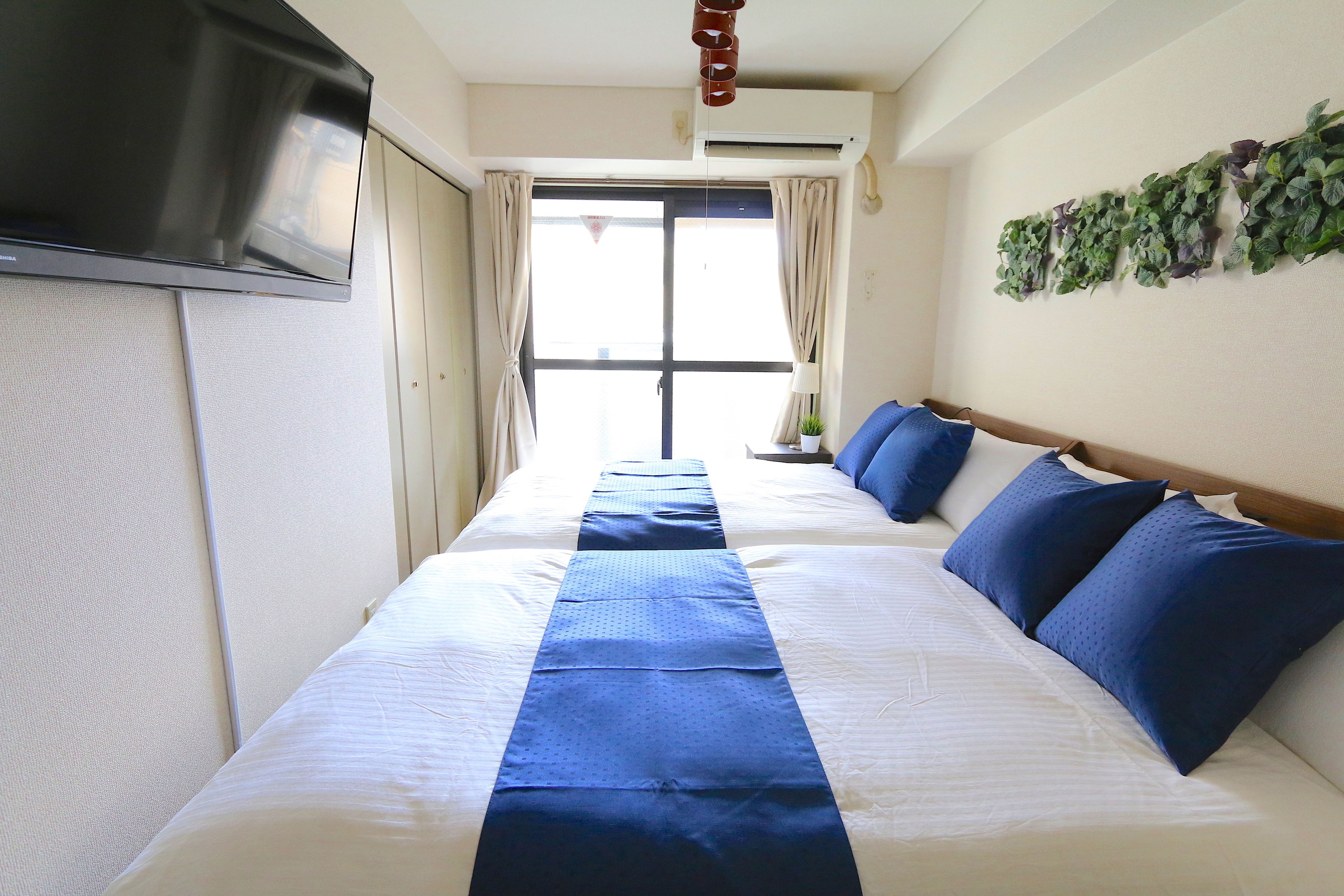 A hotel room with a large bed, a flat-screen TV mounted on the wall, and a window with curtains.