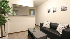 A modern living room with a black leather sofa, a small coffee table, and a potted plant. - Elizabeth Garden II (Osaka)