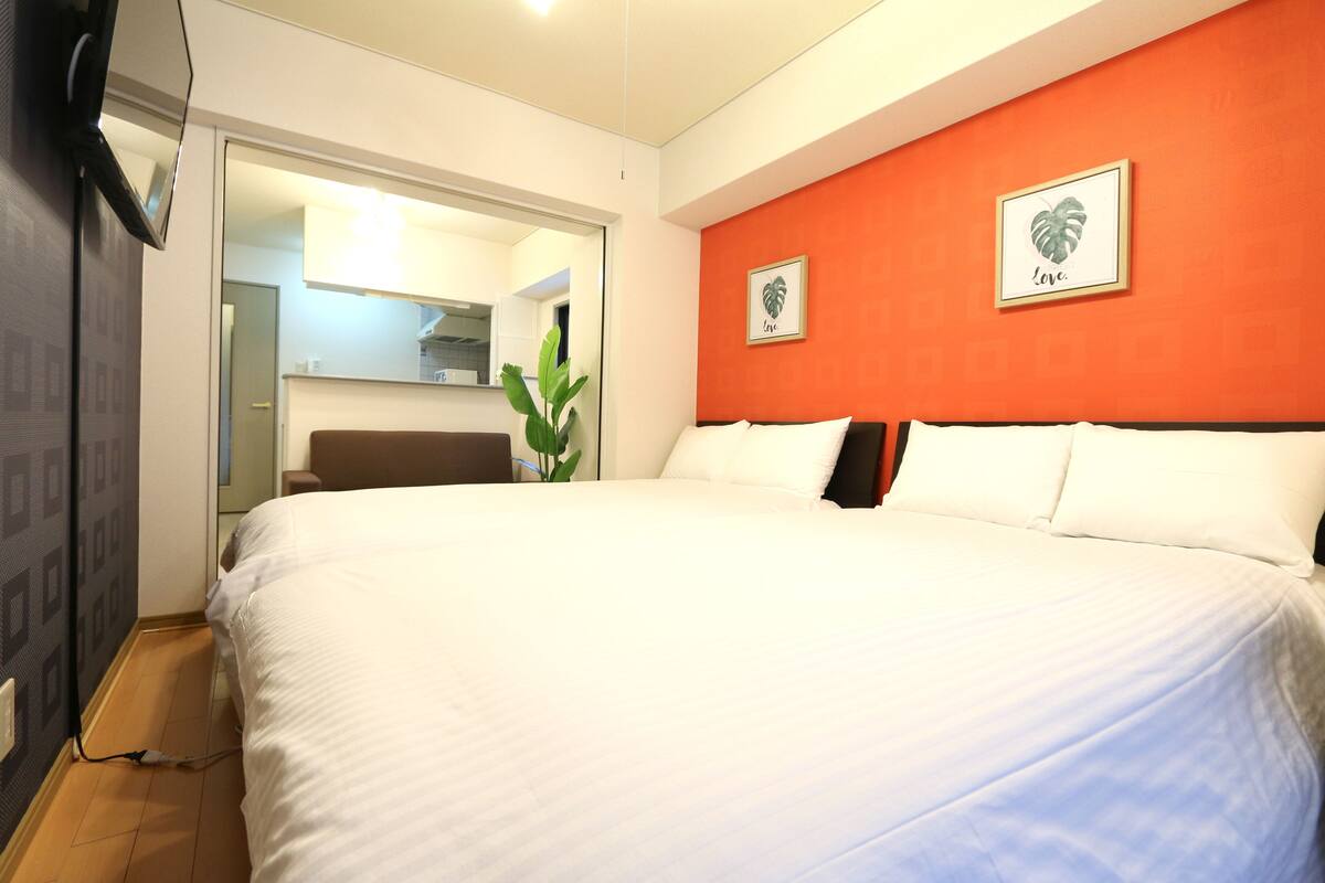 Une chambre d’hôtel avec un grand lit, un mur d’accent rouge et deux œuvres d’art représentant des feuilles, encadrées.