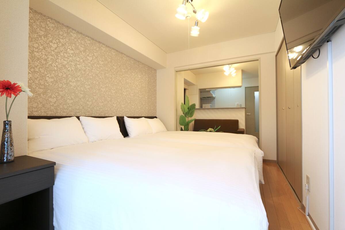 Une chambre d’hôtel avec un grand lit, une table de chevet ornée d’un vase de fleurs, un miroir et une armoire.
