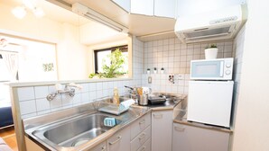 A compact kitchen with a sink, microwave, and stove. There are cabinets and a window with plants. - Elizabeth Garden II (Osaka)