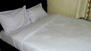 A bed with white bedding and pillows, a plain headboard, and a light-colored wall. - Bunyonyi Inn Hotel (Kampala)