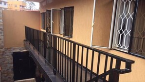 A corridor with a black railing, doors with metal bars, and windows with white frames. - Bunyonyi Inn Hotel (Kampala)