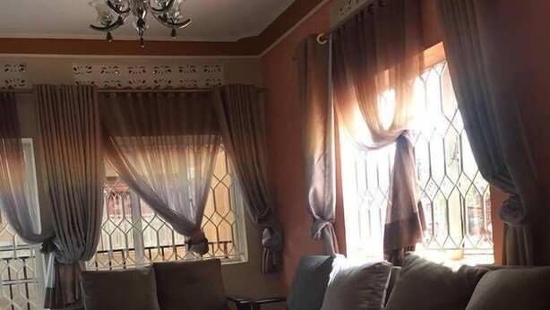 A living room with a sofa set, a chandelier, and a window with curtains. - Bunyonyi Inn Hotel (Kampala)