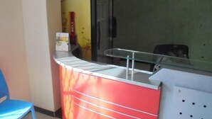 A reception desk with a glass partition, a blue chair, and a red counter. - Bunyonyi Inn Hotel (Kampala)