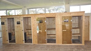 A row of wooden enclosures with benches, likely sauna or steam rooms, in a spacious indoor area with a tiled floor and large windows. - Hotel Brovad Masaka (Masaka)