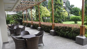 An outdoor seating area with wicker chairs and tables, surrounded by greenery and a well-maintained hedge. - Hotel Brovad Masaka (Masaka)
