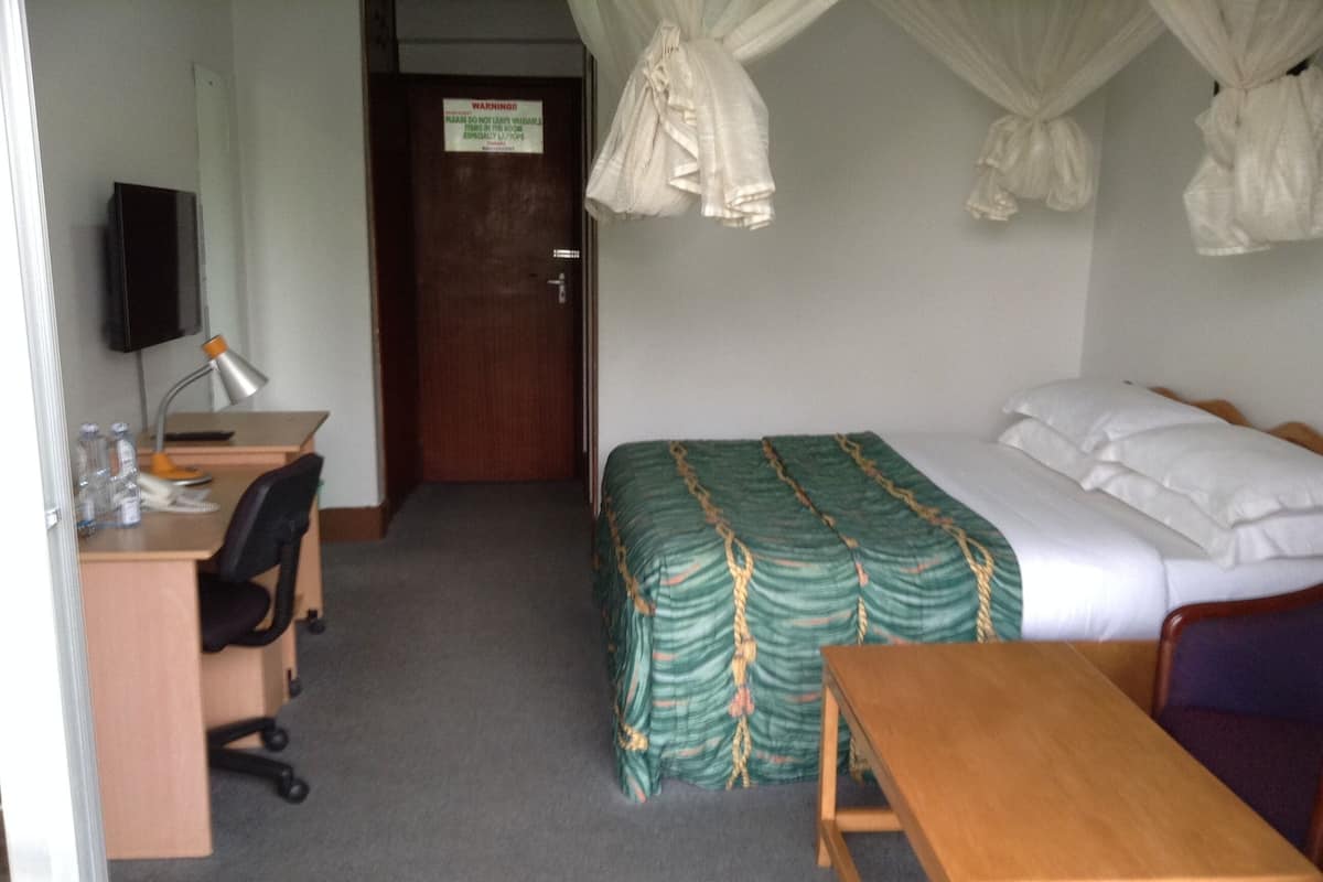 A hotel room with a bed, a desk, a chair, a table, a TV, and a door.