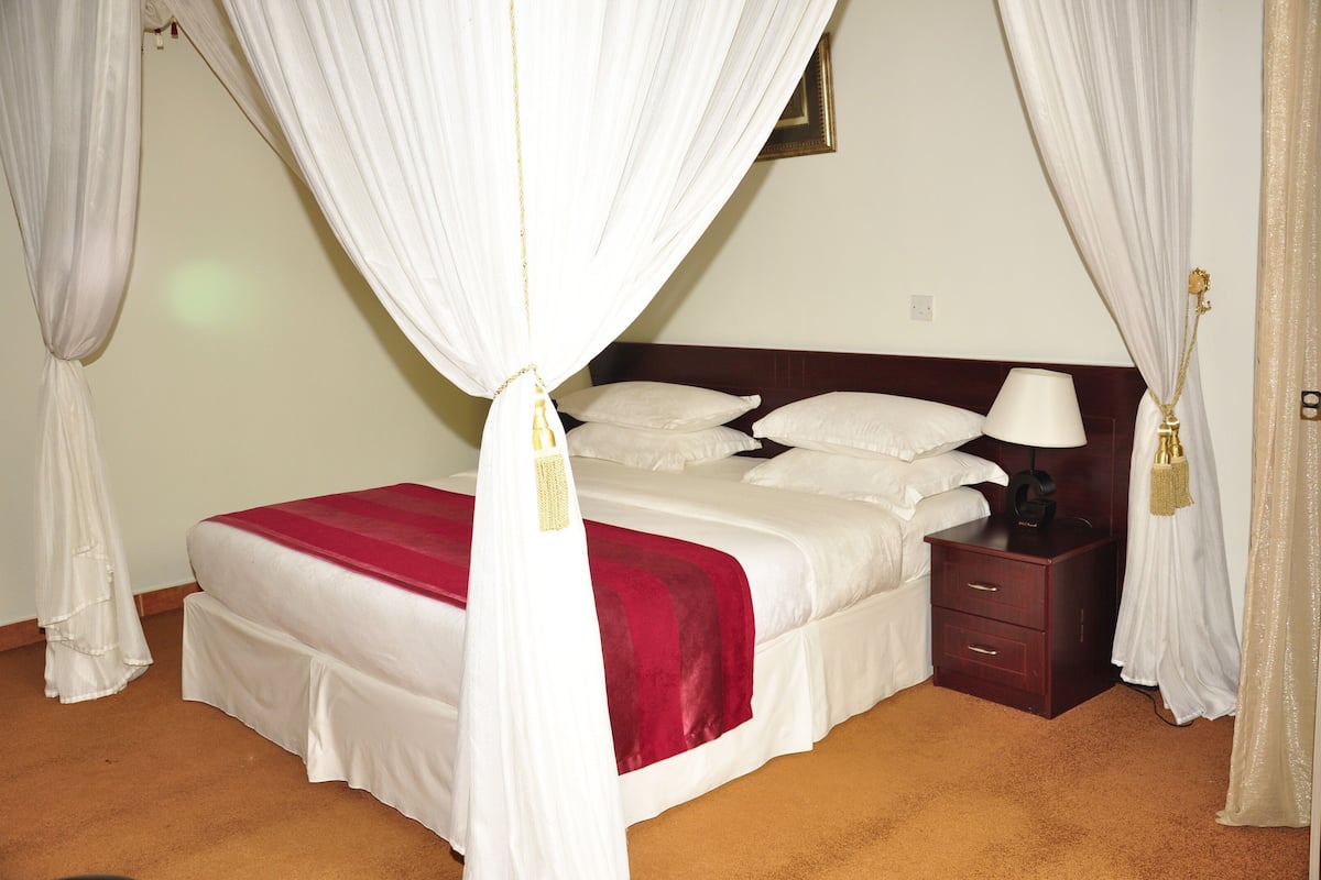 A neatly made bed with a red blanket, a bedside lamp, and a wooden nightstand.